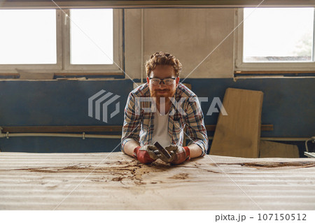 Craftsman working with chisel while cutting wooden plank in carpentry workshop and looks camera Craftsman working with chisel while cutting wooden plank in carpentry workshop and looks camera 107150512