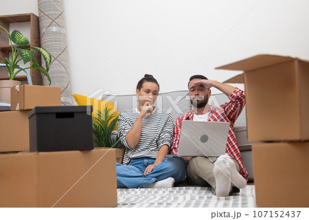 tired Couple in their home, laptop amidst boxes, online decor shopping after moving in creating their ideal sanctuary or coordinating their move tired Couple in their home, laptop amidst boxes, online decor shopping after moving in creating their ideal sanctuary or coordinating their move 107152437
