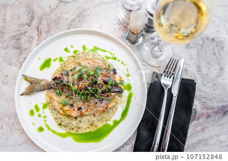 Sea bass in cream sauce with Provencal herbs and green oil on a white plate 107152848