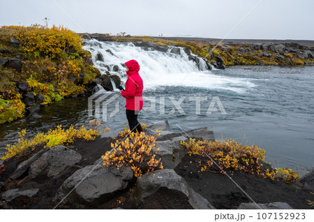 Woman in red raincoat at Grafarlandsfoss falls in northern Iceland highlands. Woman in red raincoat at Grafarlandsfoss falls in northern Iceland highlands. 107152923