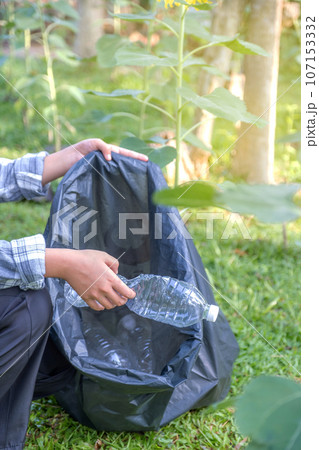 Hand holding plastic bottle waste, picking up trash putting to the black garbage bag at Sunflower Park on Environmental Earth day 107153332