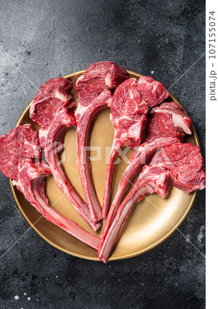 Lamb chop rib steak, raw mutton meat cutlet in golden plate. Black background. Top view Lamb chop rib steak, raw mutton meat cutlet in golden plate. Black background. Top view 107155074
