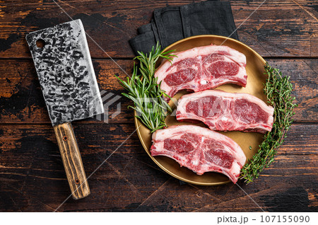 Uncooked Raw lamb loin chops steaks, saddle in plate with rosemary and thyme. Wooden background. Top view Uncooked Raw lamb loin chops steaks, saddle in plate with rosemary and thyme. Wooden background. Top view 107155090
