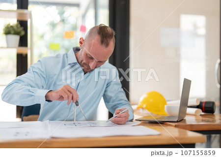 Architect caucasian male working with laptop and blueprints, engineer inspection in workplace for architectural plan, sketch a construction project Architect caucasian male working with laptop and blueprints, engineer inspection in workplace for architectural plan, sketch a construction project 107155859