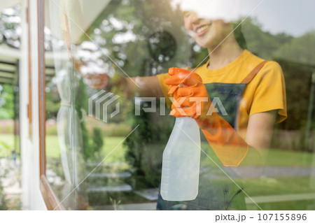 Young Asian housewife cleaning window glass with rags and detergent spray, cleaning house on the weekend 107155896