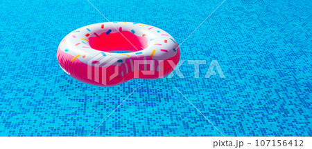 inflatable ring in the form of a donut with pink glaze in the pool in the bright sun. summer vacation, tan inflatable ring in the form of a donut with pink glaze in the pool in the bright sun. summer vacation, tan 107156412