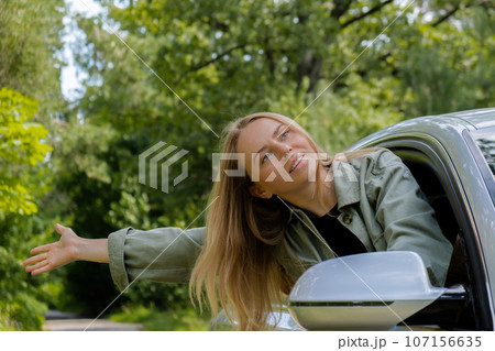 Blonde woman sticking head out of windshield car. Young tourist explore local travel making candid real moments. True emotions expressions of getting away and refresh on open clean air 107156635