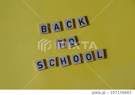 Educational greeting announcement for students and teacher. Saying BACK TO SCHOOL text on wooden blocks on colorful yellow background. Top view flat lay Concept of new school year 107156665