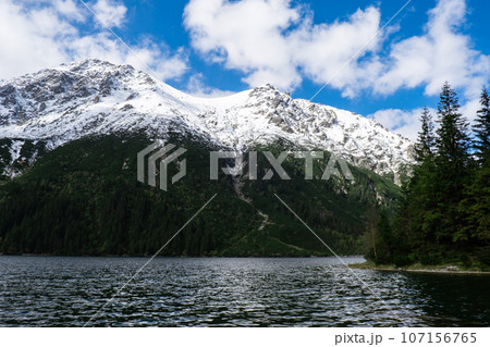 Morskie Oko lake Snowy Mountain Hut in Polish Tatry mountains, Zakopane, Poland. Beautiful green hills and mountains in dark clouds and reflection on the lake Morskie Oko lake 107156765