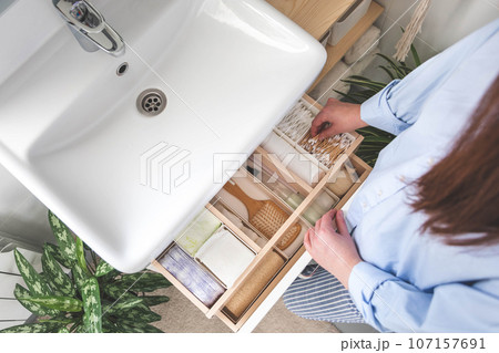 Top view of woman hands neatly organizing bathroom amenities and toiletries in drawer in bathroom. 107157691
