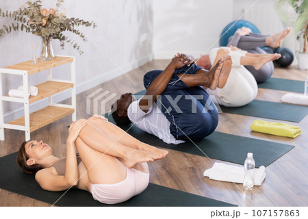 Multinational women and men practicing upward boat pose of yoga on black mat in fitness room 107157863