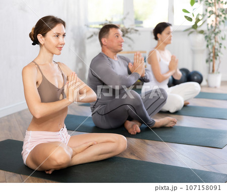 Yoman sitting in Padmasana with hands in namaste during group yoga class 107158091