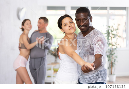 Positive woman and African american man practicing bachata dance moves in pair during group class 107158133