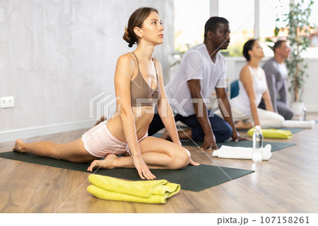 Woman practicing stretching asana Ardha Kapotasana during group yoga 107158261