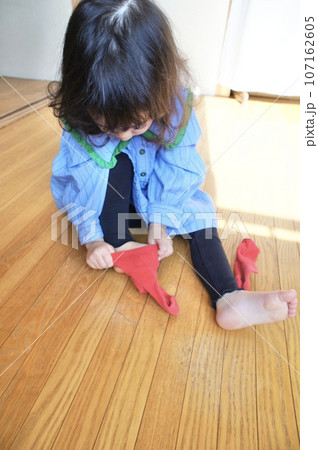 自分で赤い靴下を履く小さな女の子 自分で赤い靴下を履く小さな女の子 107162605