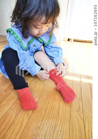 自分で赤い靴下を履く小さな女の子 107162693