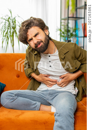 Arabian man sits on sofa feeling sudden strong abdominal stomach ache, gastritis problem, diarrhea Arabian man sits on sofa feeling sudden strong abdominal stomach ache, gastritis problem, diarrhea 107163861