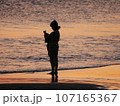 夕日に染まる海と女性 107165367