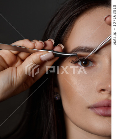 beautiful woman holding eyelashes tweezers on black background beautiful woman holding eyelashes tweezers on black background 107168818