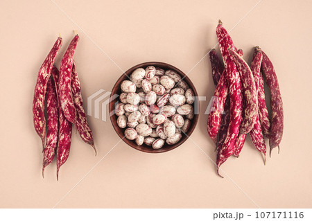 Cranberry beans. Borlotti bean pods in bowl. Top view. Stylish modern food background. Magenta color. Creative foodstuff flat lay. Grocery, dietary backdrop. Advertising, trendy magazine publication. 107171116