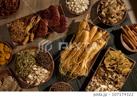 Precious traditional medicines are displayed on wooden trays on vintage wooden background. Scene for advertising product with natural ingredient: ginseng, ganoderma, ginger, cinnamon 107174322