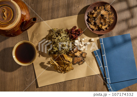 Top view of medicine cup, medicine package and dried herbs decorated on wooden table background. Collection of herbs to prepare a tonic drink, traditional medicine from China. Advertising photo Top view of medicine cup, medicine package and dried herbs decorated on wooden table background. Collection of herbs to prepare a tonic drink, traditional medicine from China. Advertising photo 107174332