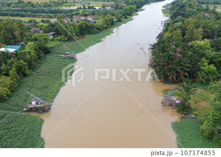 Aerial view of fishing trap net in canel with fisherman urban city village town houses, lake or river. Nature landscape fisheries and fishing tools at Pak Pha, Songkhla, Thailand. Aquaculture farming Aerial view of fishing trap net in canel with fisherman urban city village town houses, lake or river. Nature landscape fisheries and fishing tools at Pak Pha, Songkhla, Thailand. Aquaculture farming 107174855