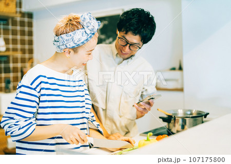 スマホを見ながら料理をするカップル（夫婦） 107175800