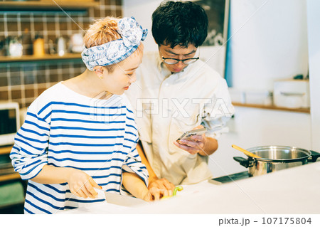 スマホを見ながら料理をするカップル(夫婦) スマホを見ながら料理をするカップル(夫婦) 107175804