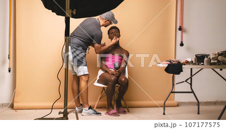 Visagiste applying lipstick while doing makeup on transgender preparing for photo shoot 107177575