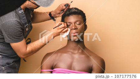 Visagiste applying lipstick while doing makeup on transgender preparing for photo shoot Visagiste applying lipstick while doing makeup on transgender preparing for photo shoot 107177576