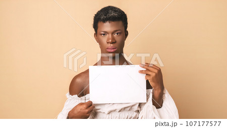 Transgender person looking at camera with serious face while holding a blank white paper. 107177577