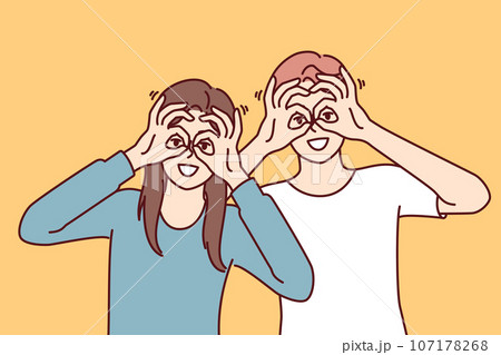 Funny man and woman make binoculars from fingers and look at screen smiling to cheer friends. 107178268
