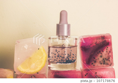 Cosmetic serum glass bottle with pipette on ice cubes with fresh pitaya, citrus 107178676