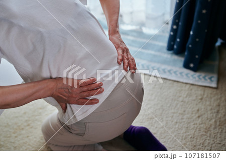 腰の痛みをこらえながら立ち上がるシニア女性 腰の痛みをこらえながら立ち上がるシニア女性 107181507