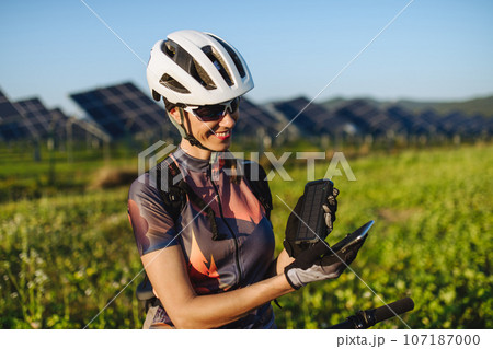 Cyclist charging her smartphone using a solar phone charger. 107187000