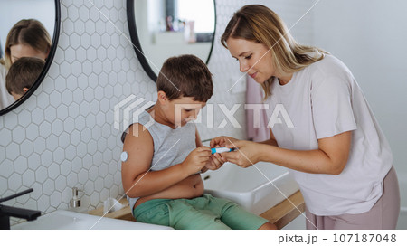 Mother of diabetic boy injecting insulin in his abdomen. 107187048