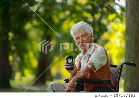 Senior diabetic man in wheelchair checking his glucose data on smartphone outdoors, in park. Senior diabetic man in wheelchair checking his glucose data on smartphone outdoors, in park. 107187163