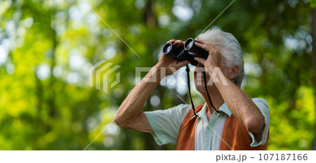 Senior man spending free time outdoors in nature, watching forest animals through binoculars. 107187166