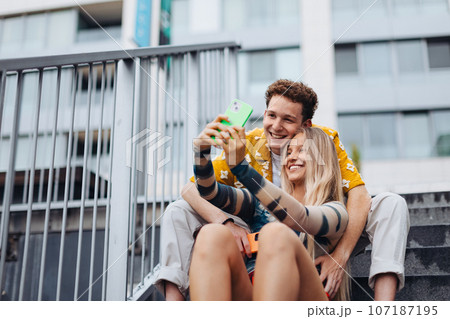Portrait of generation z couple sitting outdoors in the city and taking selfie. 107187195