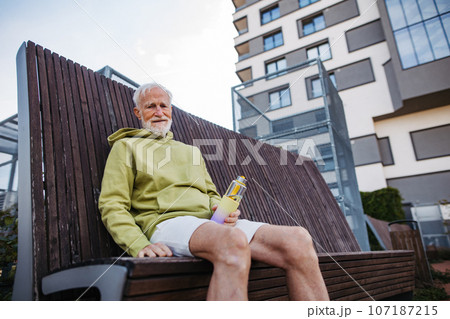 Elderly man sitting on bench, resting after his morning run. 107187215