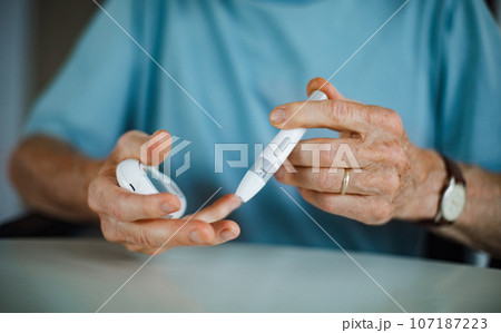 Diabetic senior man on wheelchair checking blood sugar level with fingerstick testing glucose meter. 107187223