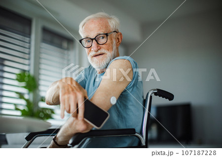 Diabetic senior man checking blood glucose level at home using continuous glucose monitor. 107187228