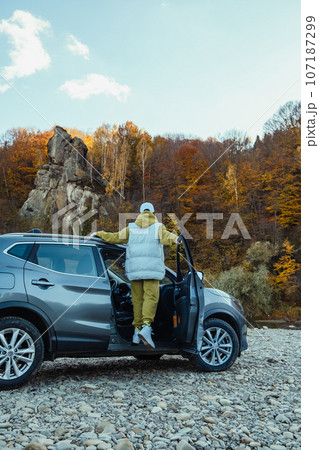 woman traveler near car at rocky beach of mountain river woman traveler near car at rocky beach of mountain river 107187299