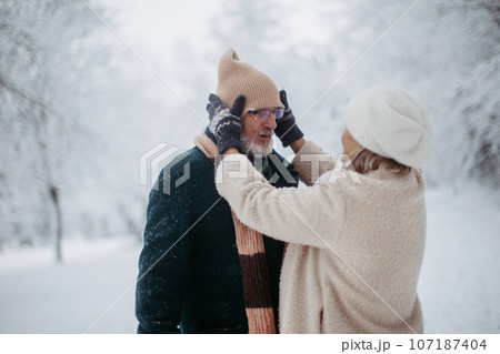 Elegant senior couple walking in the snowy park, during cold winter snowy day. 107187404