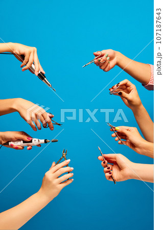 Female hands holding different tools for manicure against blue background. Cutter, scissors, nippers, cuticle push Female hands holding different tools for manicure against blue background. Cutter, scissors, nippers, cuticle push 107187643