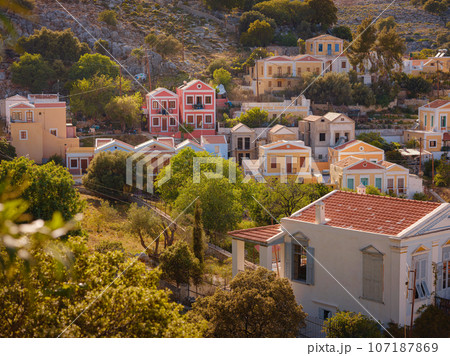Symi Island, Greece. Greece islands holidays from Rhodos in Aegean Sea. Colorful neoclassical beautiful houses on hillsides of a Greek island during sunset. Holiday travel background. 107187869