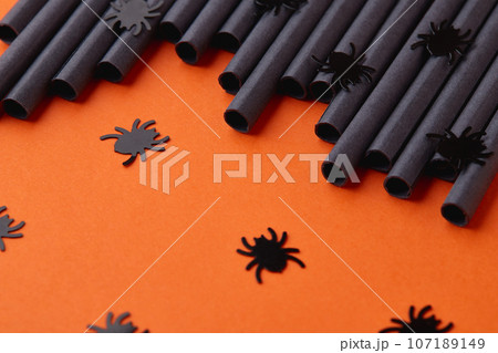 Black paper straws on orange background. Halloween party 107189149