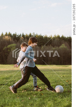 Joyful teen kicking ball while friend running...の写真素材