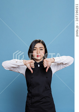 Restaurant woman employee showing thumbs down gesture, symbolizing experience discontent and dissatisfaction portrait. Asian waitress displaying disapproval concept and looking at camera 107196851